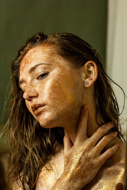 Free Close-up portrait of a woman with gold glitter makeup on face and body, posing alluringly. Stock Photo