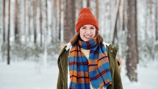 A cheerful woman in winter clothes smiles in a snowy forest setting.
