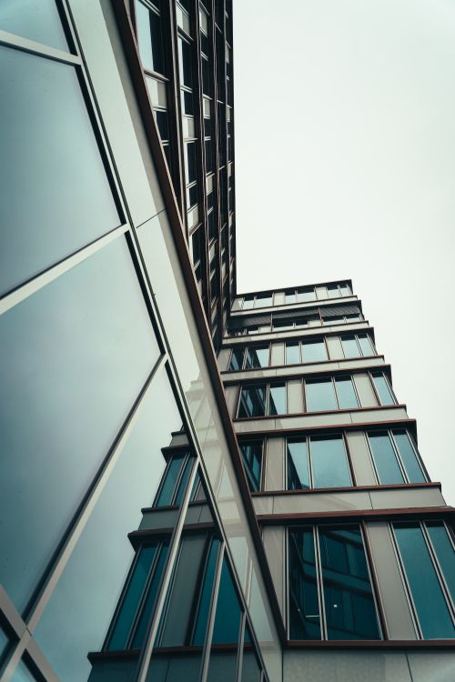 Free A striking low angle view of a modern building with glass windows reflecting the sky. Stock Photo