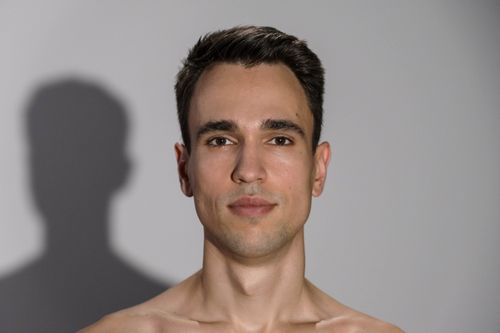 Free Portrait of a young adult man with a neutral expression in a studio setting. Soft lighting and minimal background. Stock Photo