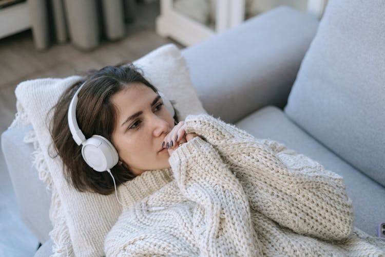 A Woman Lying Down In A Couch Wearing Headphones