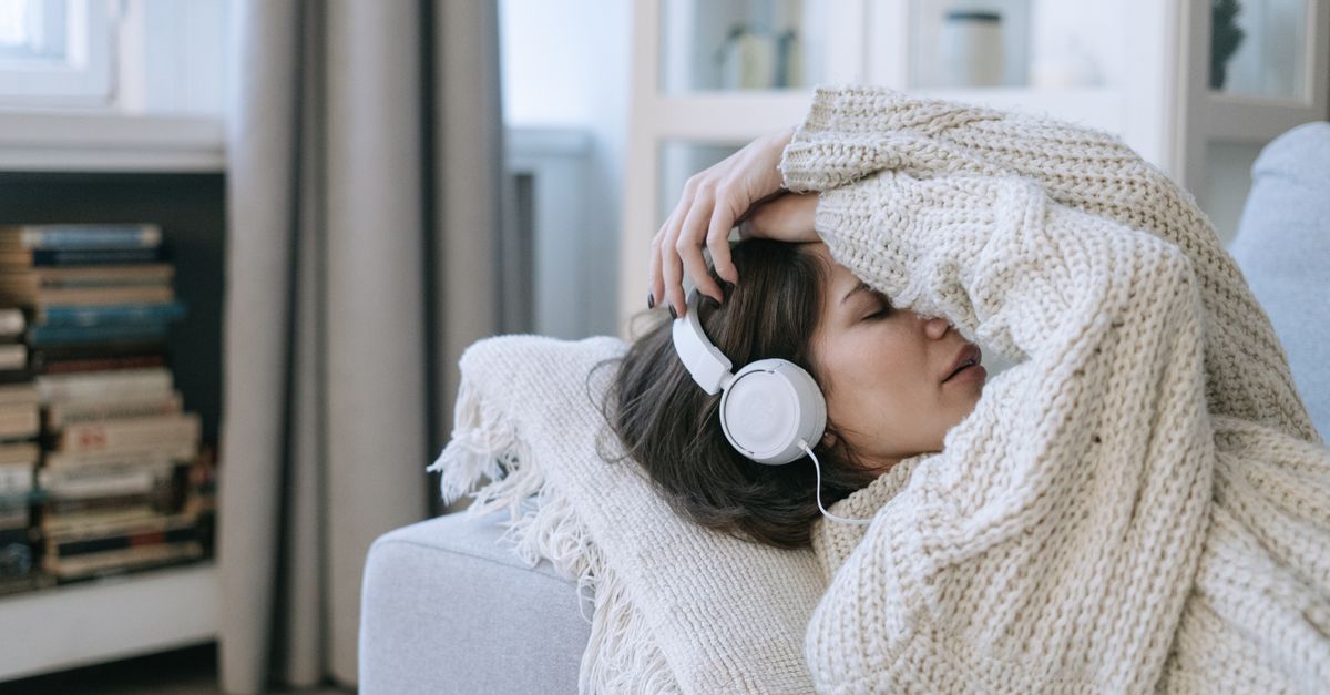 A person wearing headphones, eyes closed, with digital soundwaves flowing around their head