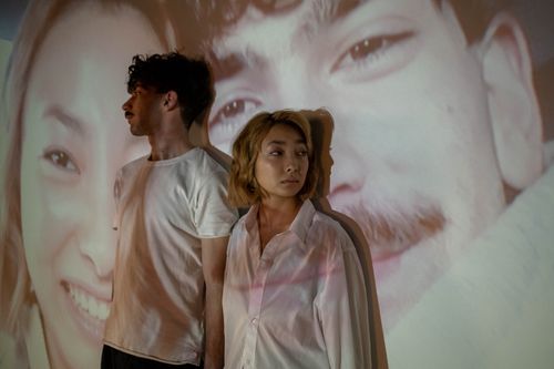 Free A couple stands with projected images on a wall, exploring identity and connection. Stock Photo