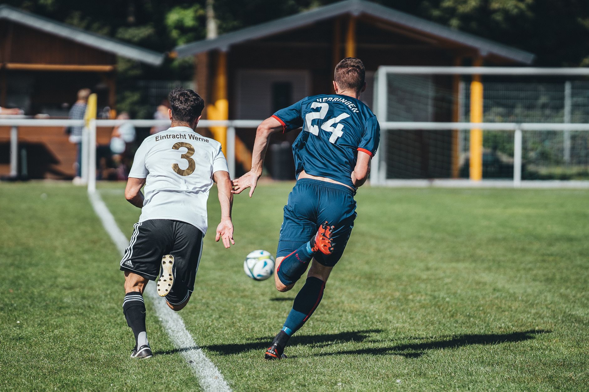 Back view anonymous professional male football players running for ball during match in outdoor stadium on sunny day