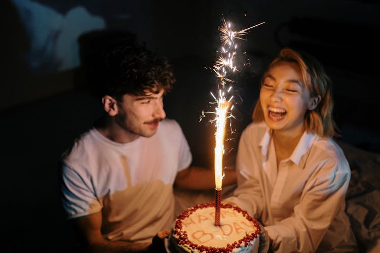 A Couple Holding A Birthday Cake With Sparkling Candle