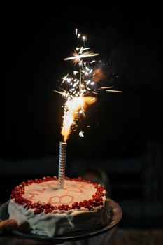 Delicious birthday cake with a sparkling candle, set against a dramatic black background.