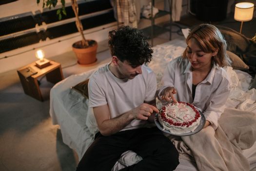 A couple enjoying a quiet birthday celebration with cake in a cozy bedroom setting.
