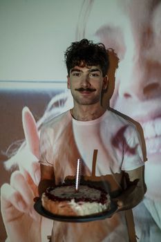 Young man with cake and projection creates a unique birthday celebration scene indoors.