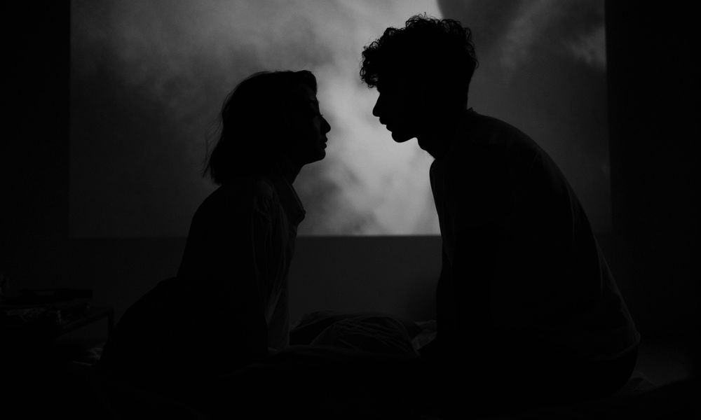 Two people sharing a quiet, candlelit moment in shadow, representing the intensity of a Destiny Matrix soulmate connection
