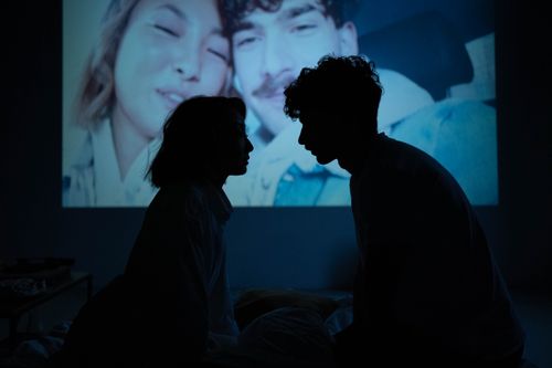 Free Silhouetted couple sitting indoors against a projected photo backdrop, creating a romantic ambiance. Stock Photo