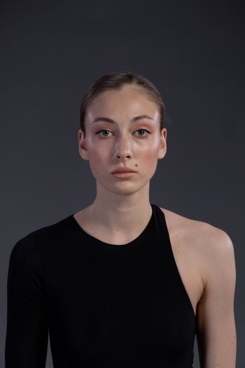 Free Sophisticated portrait of a woman in a black one-shoulder dress on a gray backdrop. Stock Photo