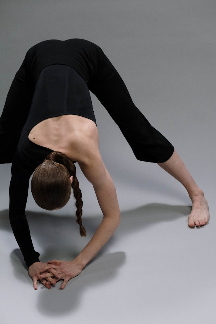 A Person In Black Clothing Bending Forward With Hands On The Floor