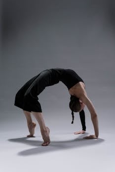 A woman performing a backbend yoga pose demonstrating flexibility and control on a gray background.