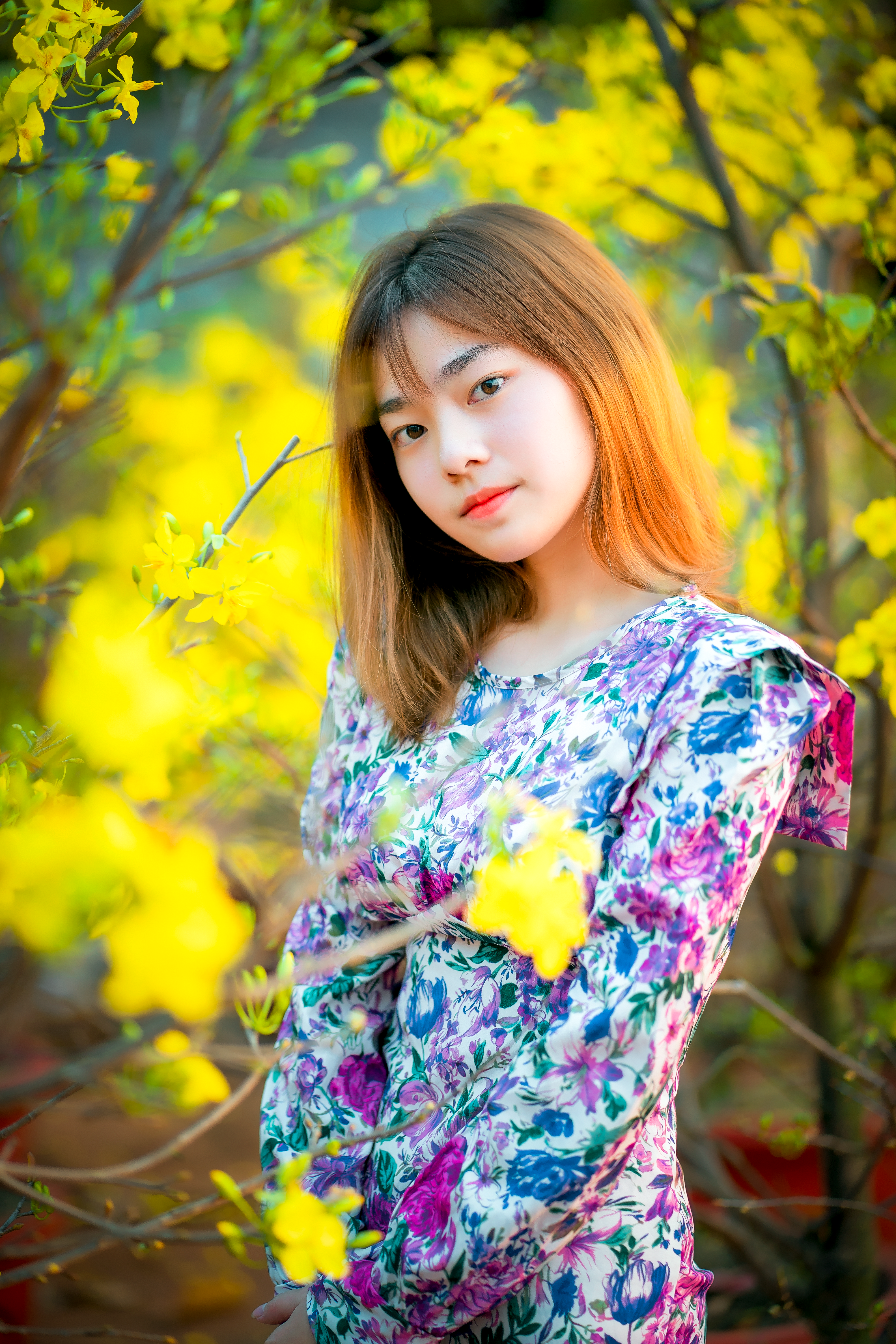 Portrait of a woman in a floral dress surrounded by vivid yellow flowers outdoors.