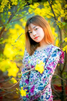 Portrait of a woman in a floral dress surrounded by vivid yellow flowers outdoors.