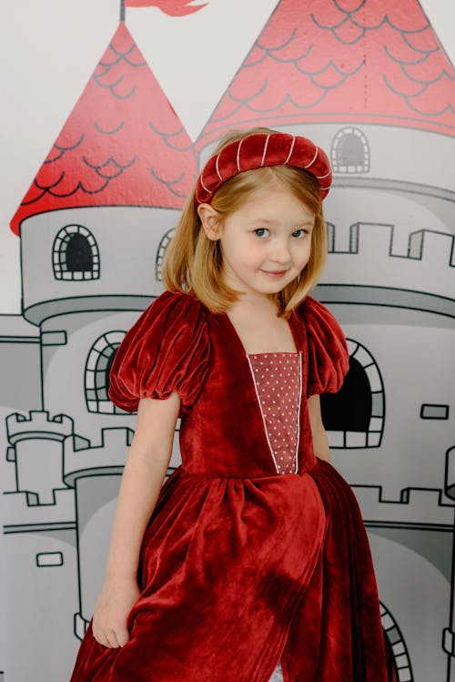 Child Wearing a Red Gown Beside a Castle Wall Painting