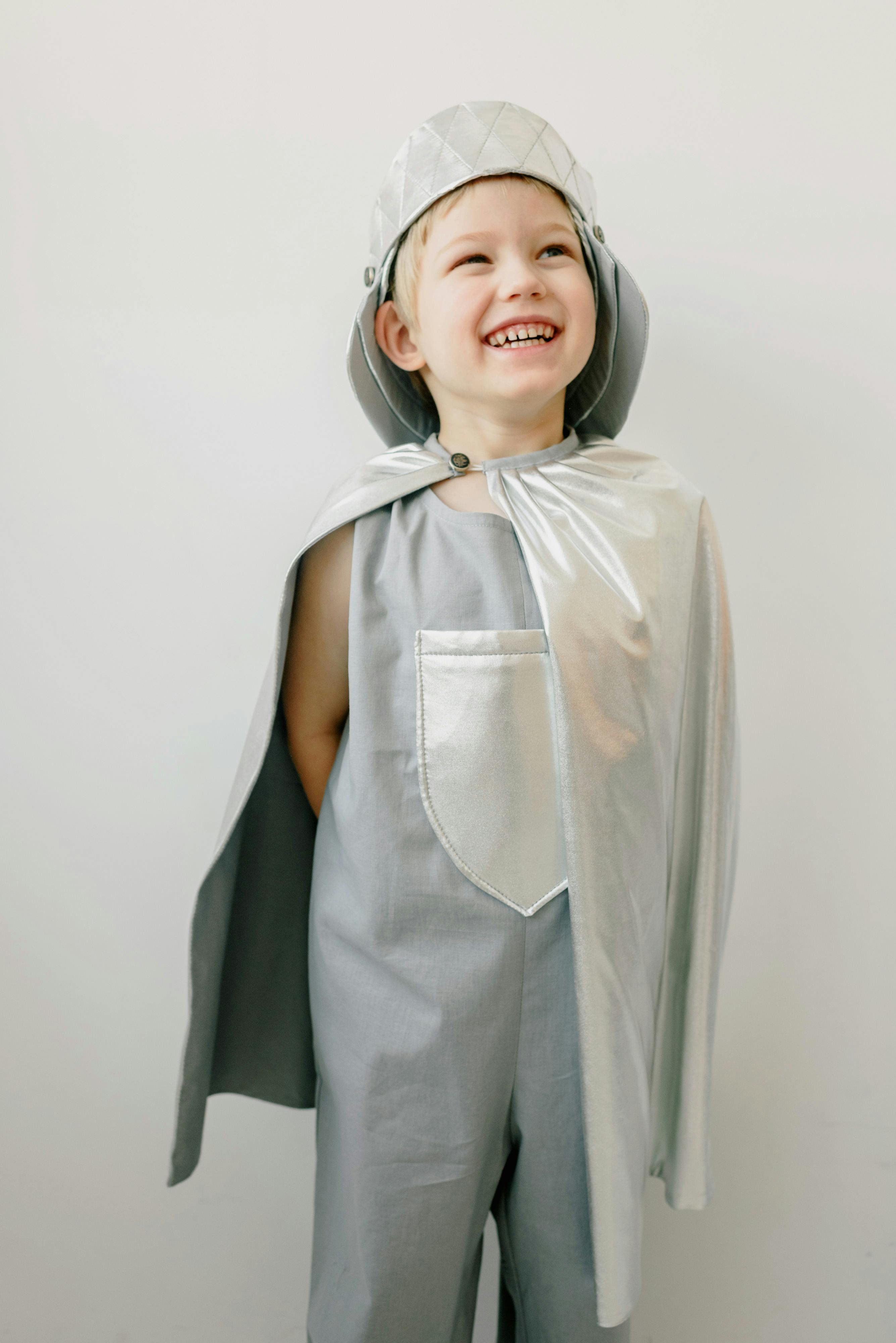 Happy young boy wearing a silver knight costume with a cape indoors