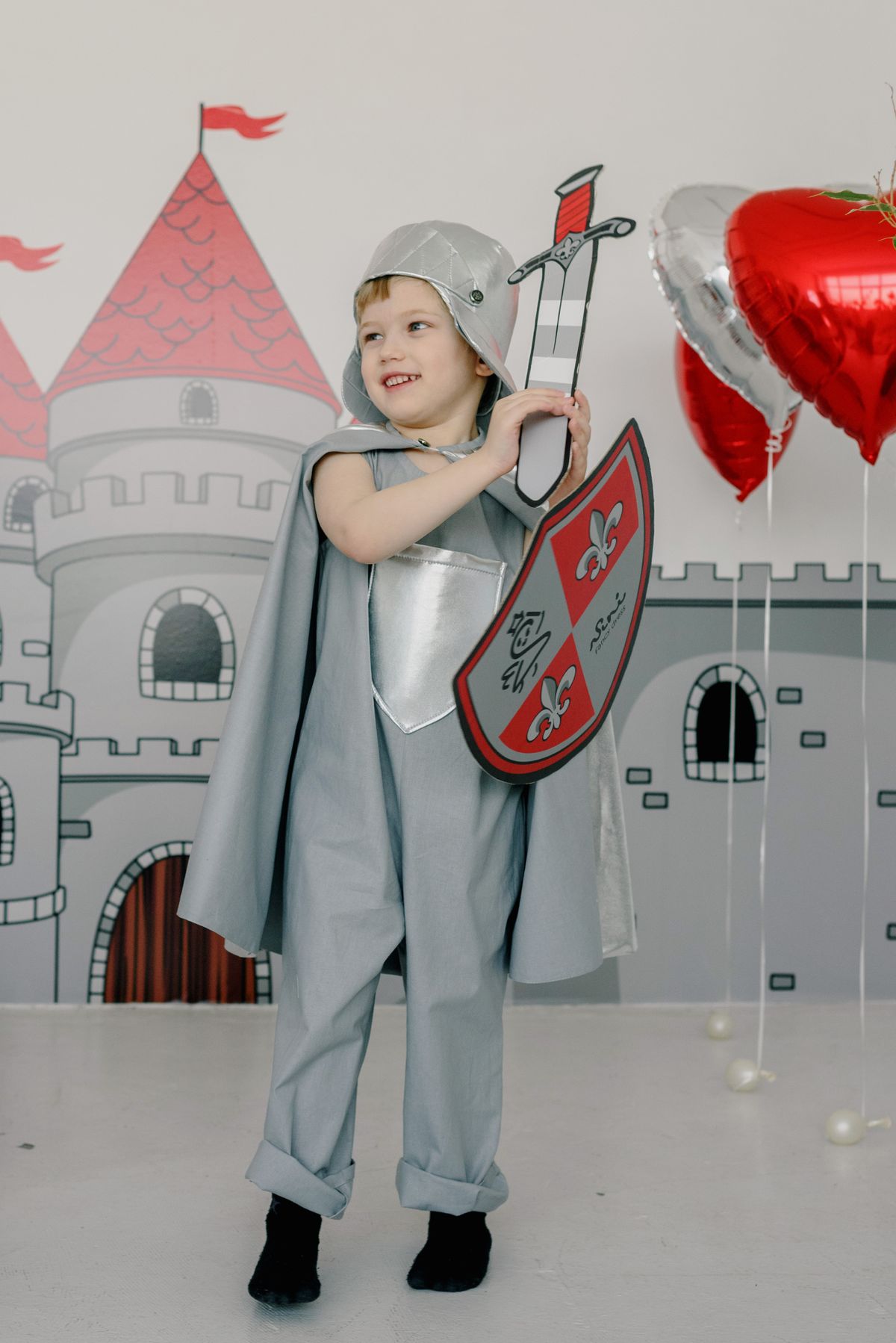 Child in a knight costume holding a shield in front of a castle backdrop