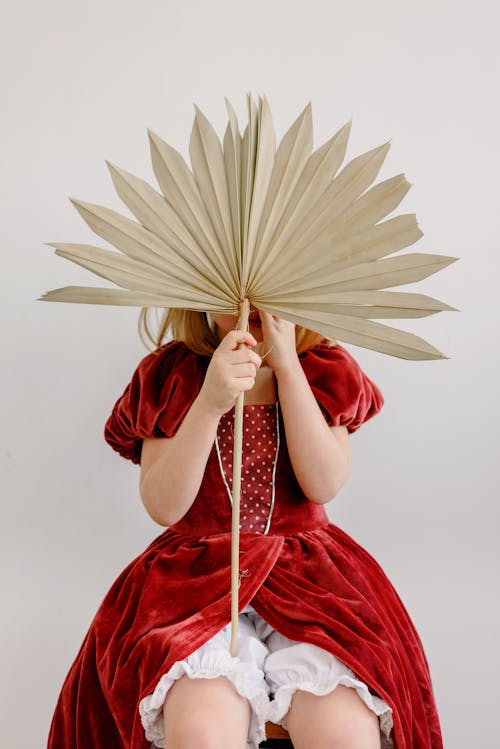 A Girl Wearing a Red Dress Hiding behind a Dry Palm Leaf