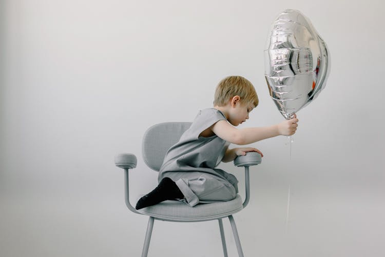 Child Sitting On A Chair Holding A Balloon