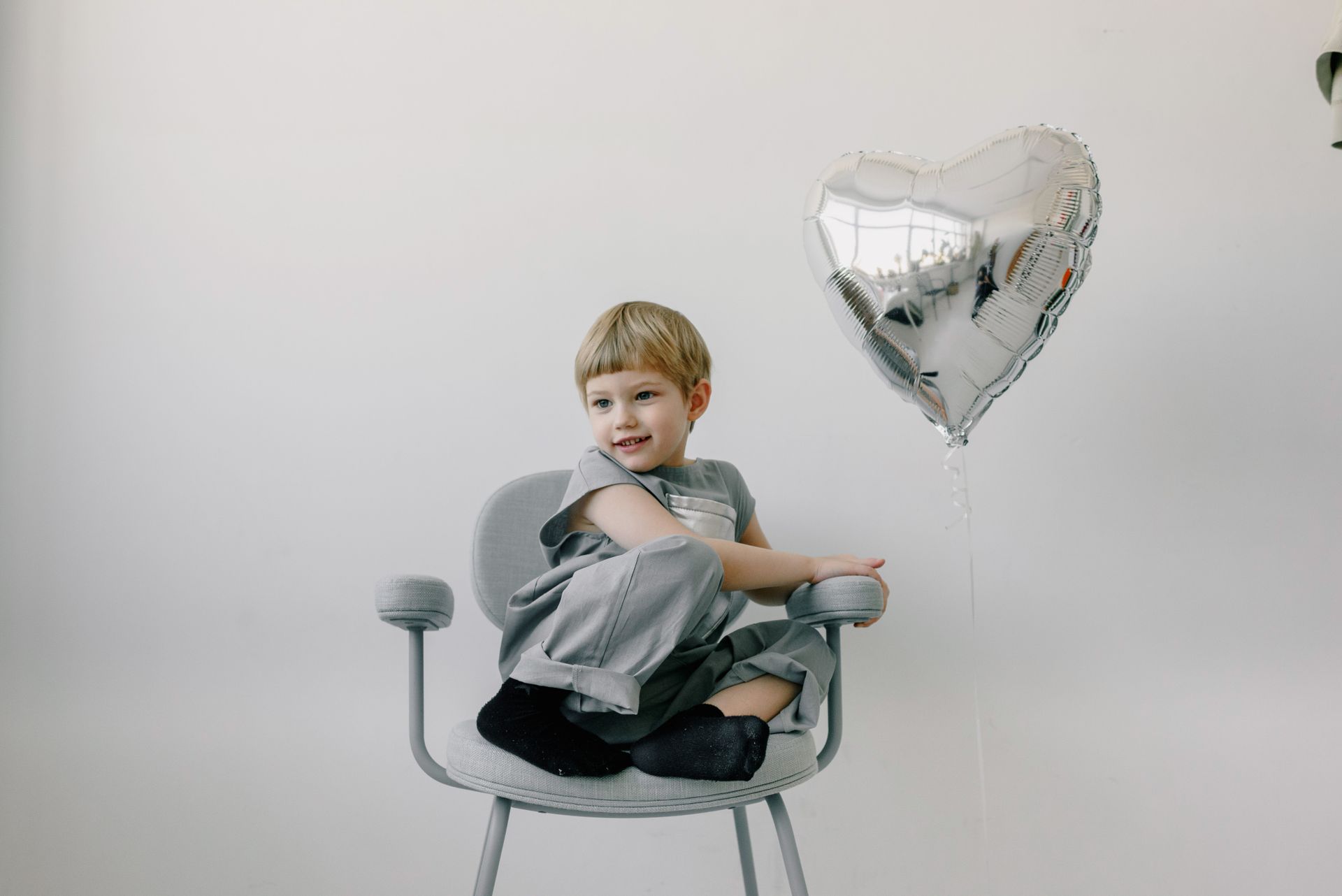 A Kid Sitting on a Chair Near a Silver Balloon