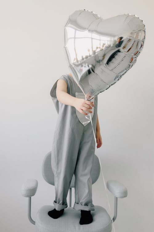 Free Child Standing on a Chair Holding a Balloon Stock Photo