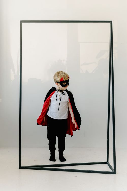 Free A young child dressed as a superhero stands inside a frame in a studio setting, exuding creativity and imagination. Stock Photo