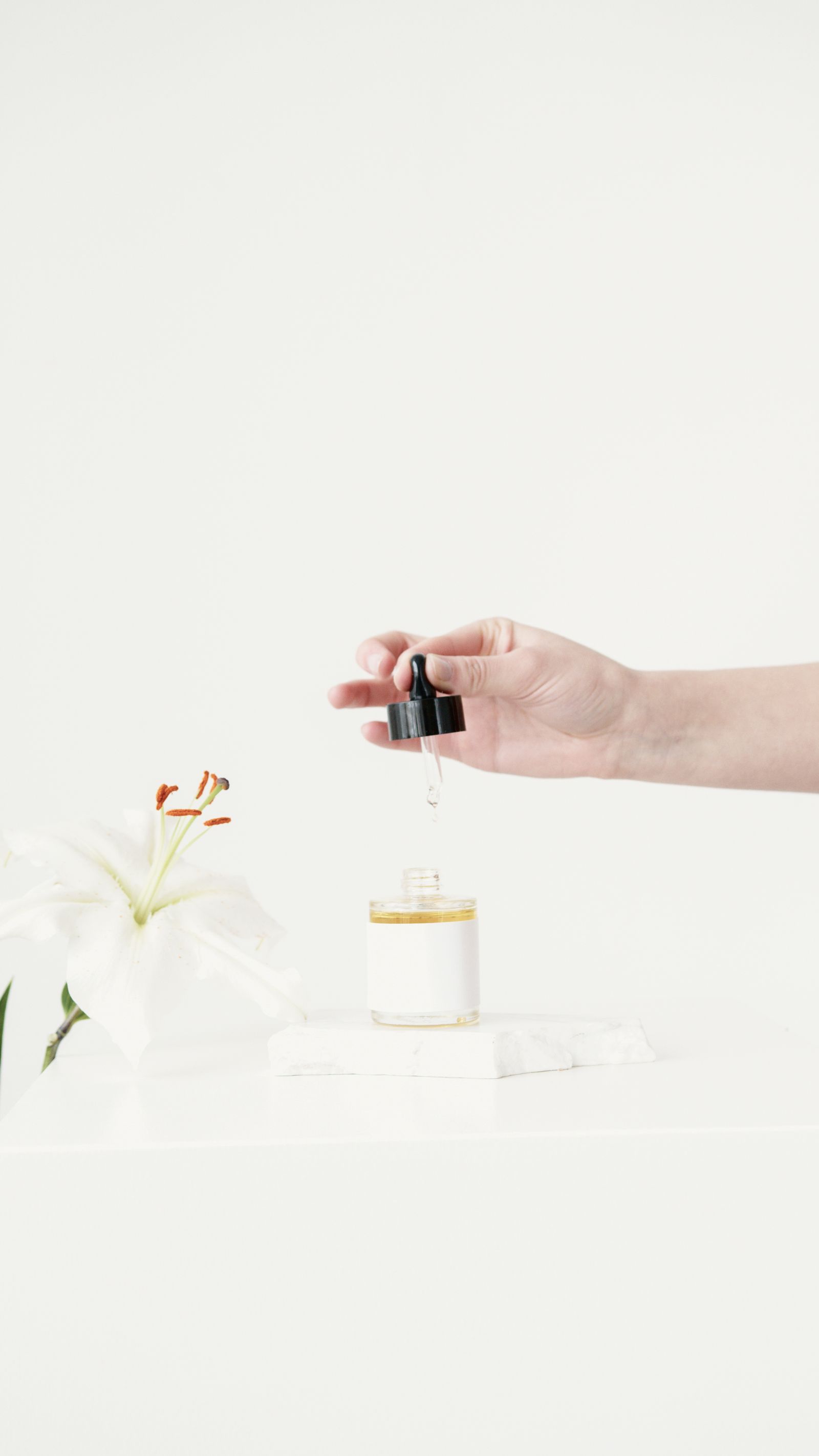 Dropper bottle beside a lily on a bright clean surface.