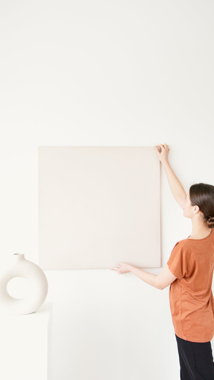 A Woman Hanging A Frame On The Wall