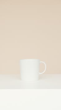 A simple and elegant white ceramic mug displayed on a neutral beige background, showcasing minimalist design.