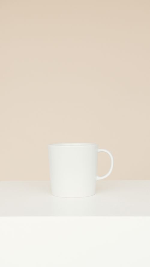 Free A simple and elegant white ceramic mug displayed on a neutral beige background, showcasing minimalist design. Stock Photo