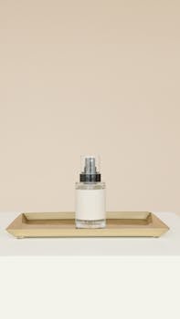 Elegant moisturizer in a glass dispenser placed on a gold tray against a beige backdrop.