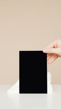 A hand holding a blank black card against a beige minimalist background, ready for mockup.