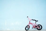 一辆粉红色的儿童自行车倚在简单的蓝色墙边，营造出异想天开的城市场景