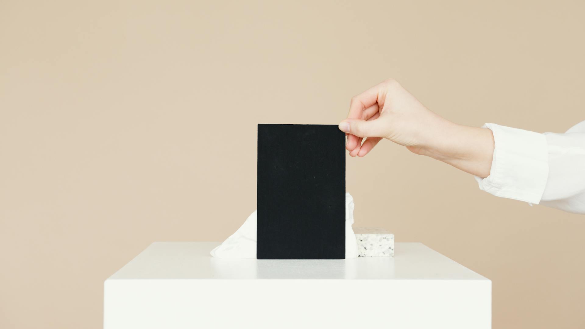 A minimalist composition featuring a hand holding a black card against a beige background with ample copyspace.