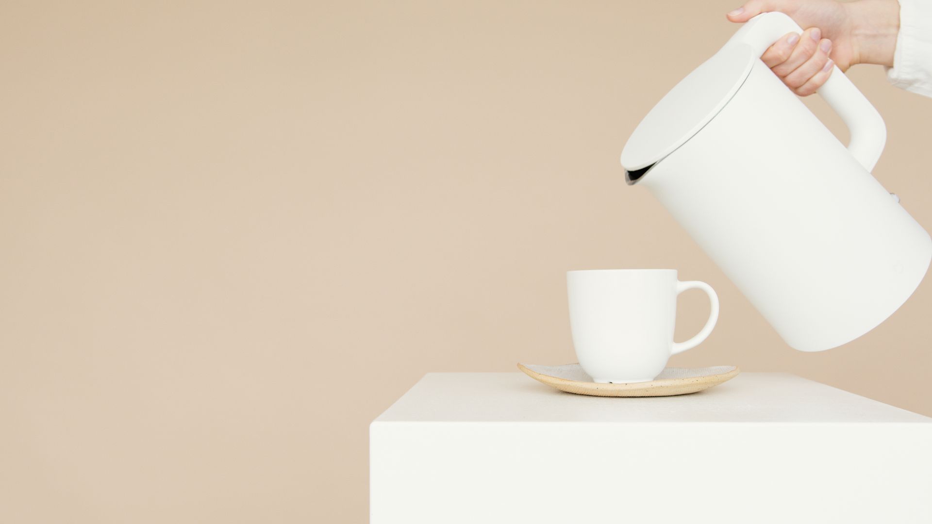Simple minimalist image of a white kettle pouring into a matching cup and saucer.