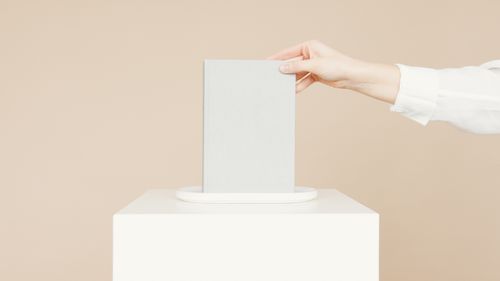 Free A hand places a blank book on a pedestal against a neutral background, perfect for mockups. Stock Photo