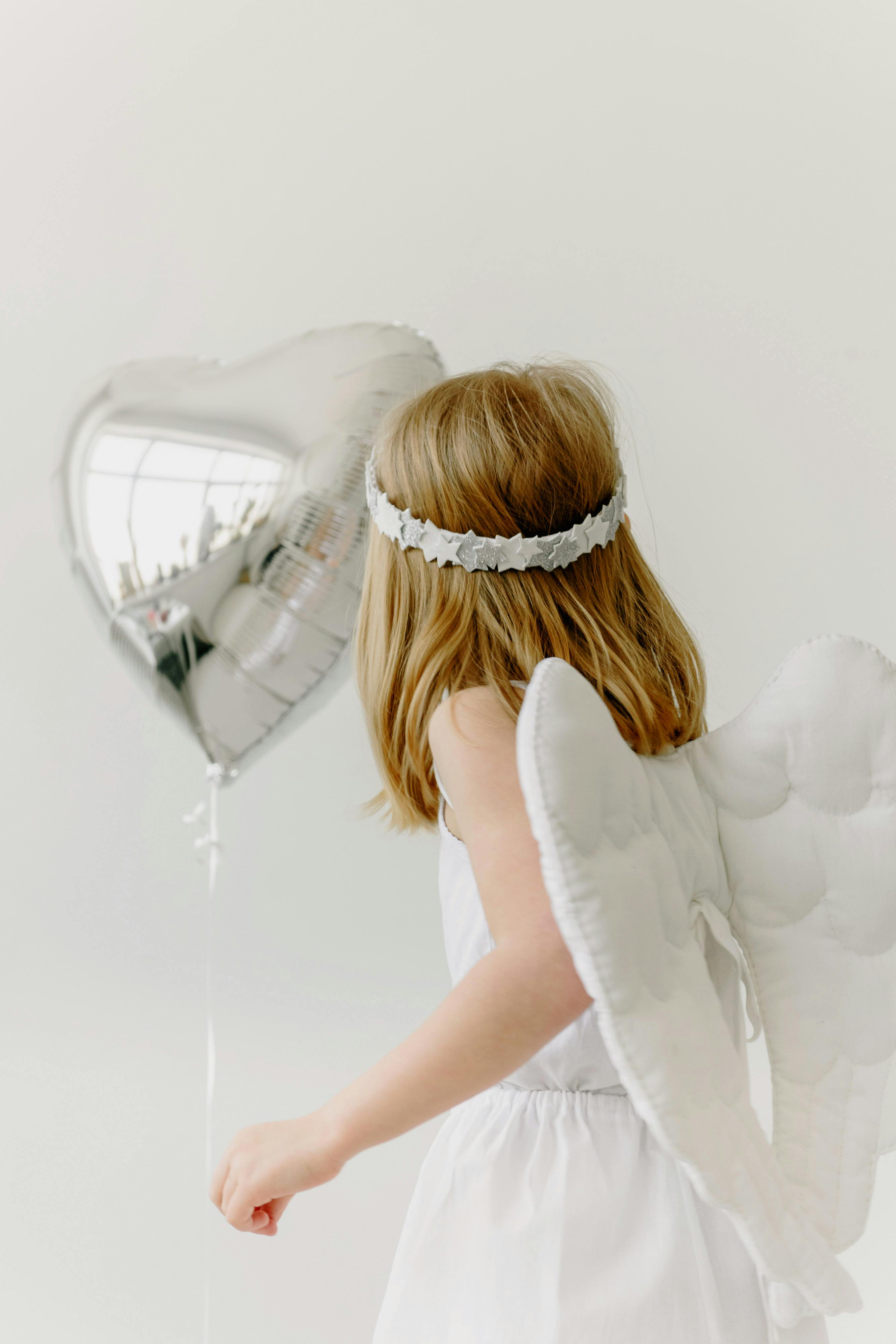 girl in an angel costume holding a silver balloon