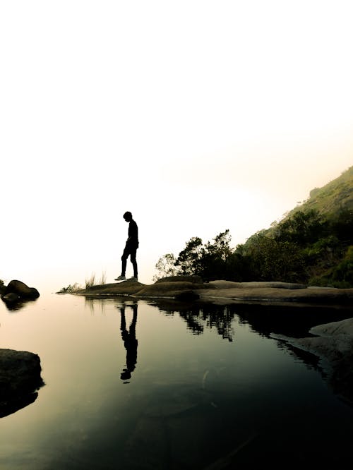 Free Silhouette of Person Standing on Rock Near Body of Water Stock Photo