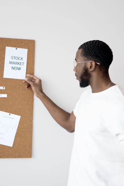 Businessman in white analyzing stock market insights on a corkboard. Businessman in white analyzing stock market insights on a corkboard.