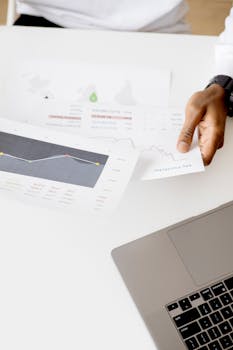 Person analyzing business reports with charts on a laptop in a modern office setting.