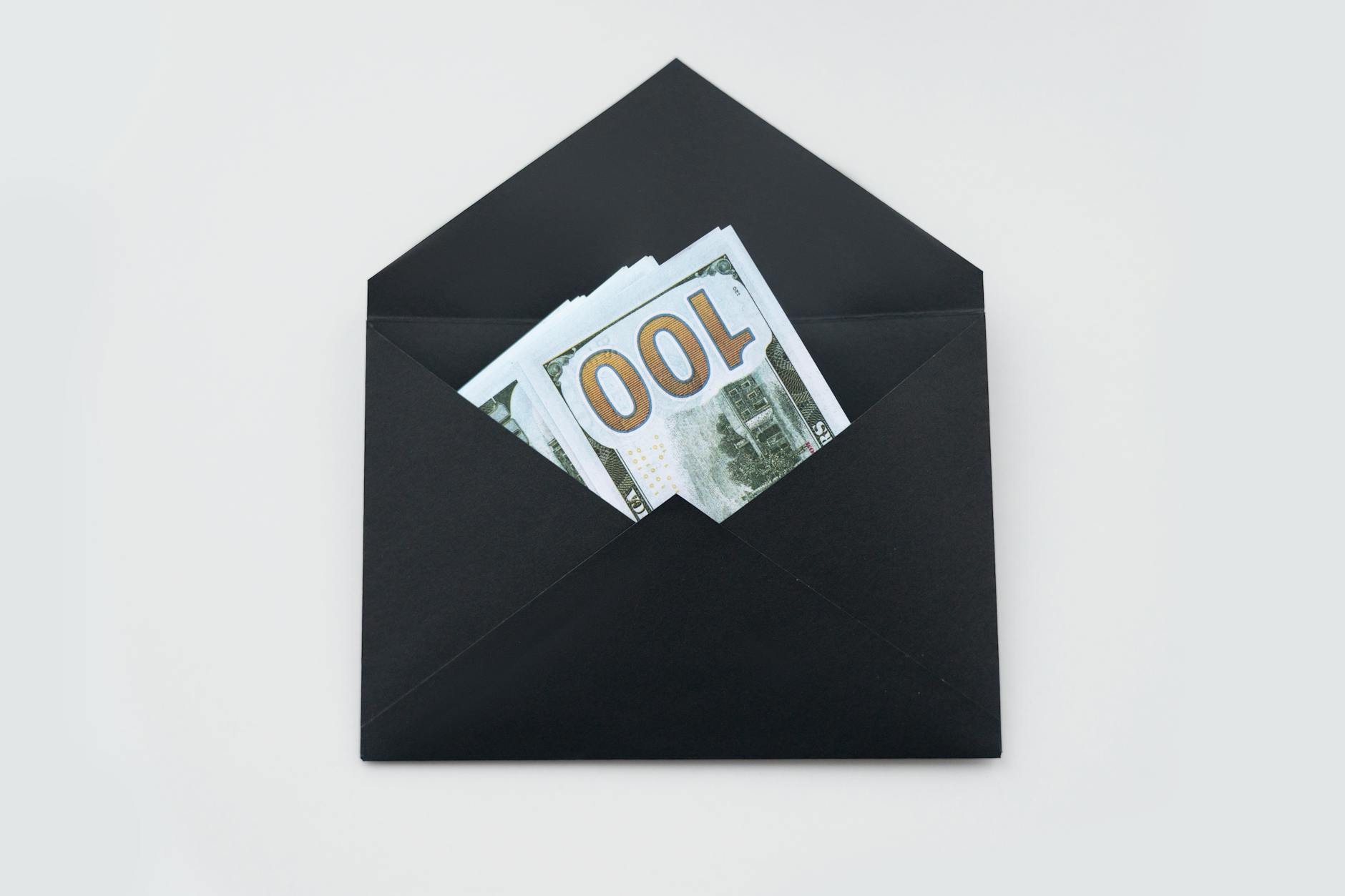 FD vs Mutual Funds: Which One Gives You Better Returns? 4 Hundred dollar bills partially visible in an open black envelope on a white background.