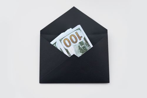 Free Hundred dollar bills partially visible in an open black envelope on a white background. Stock Photo