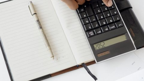 A hand using a calculator with financial documents and notebook, depicting an office setup for financial analysis.