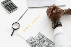 Hands folded over stock market documents with calculator and cash on desk.