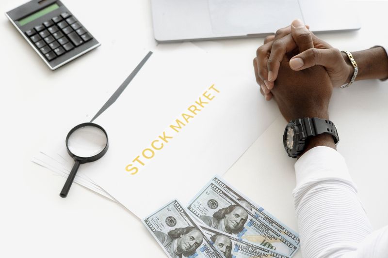 Hands folded over stock market documents with calculator and cash on desk.