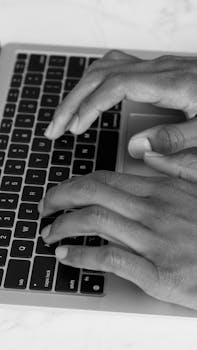 Monochrome shot of hands typing on a laptop keyboard, emphasizing technology and productivity.