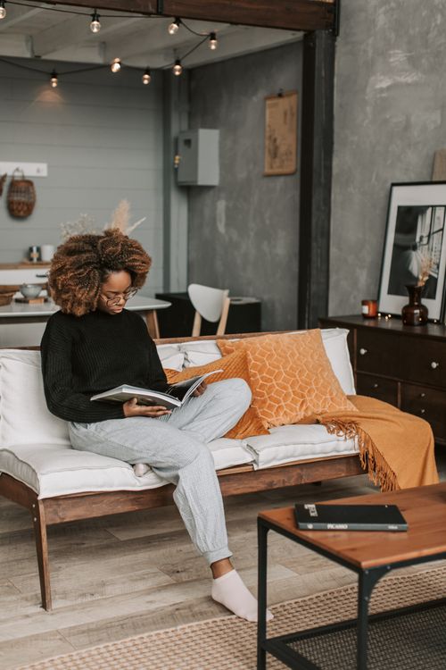 Free A young woman with afro hair relaxes on a couch while reading a magazine in a stylish modern living room. Stock Photo