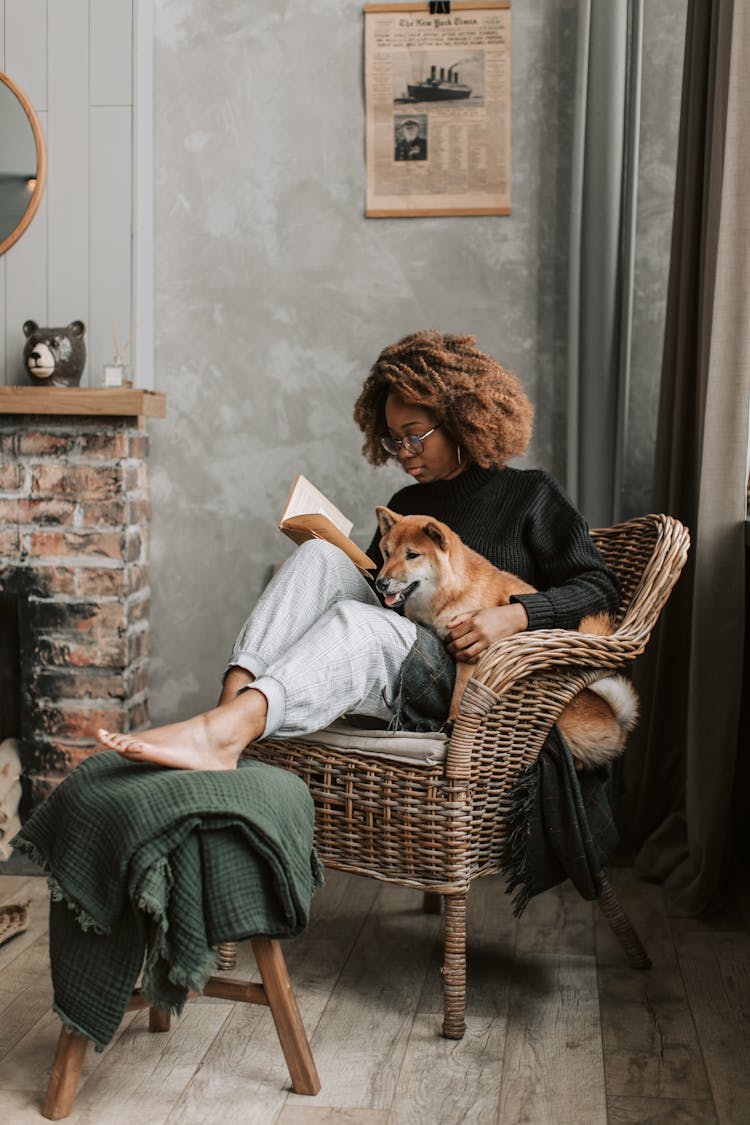 Woman Relaxing At Home While Reading A Book With Her Dog