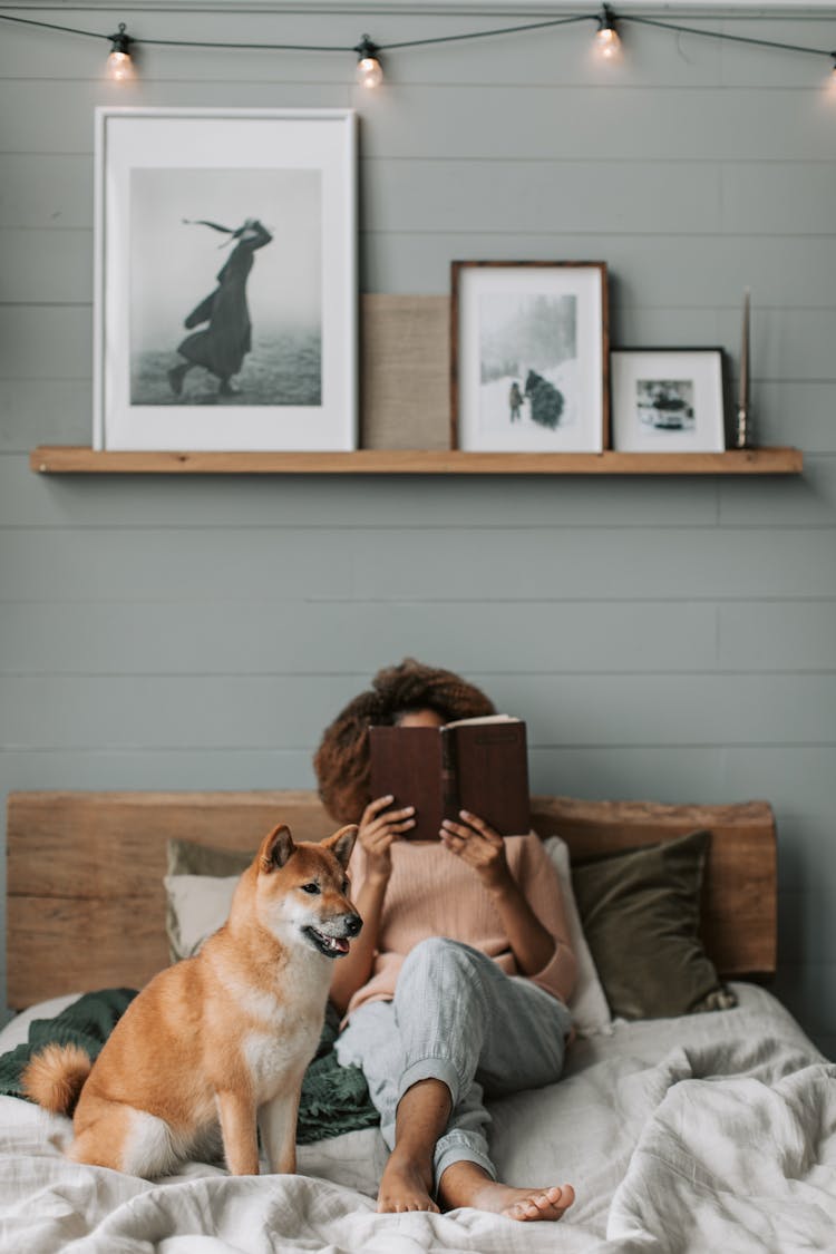 A Woman Reading A Book Beside Her Dog 